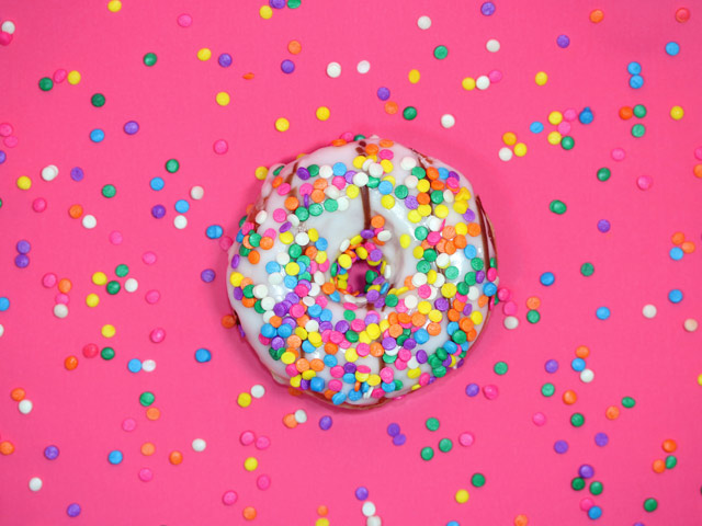 Glazed doughnut on a pink background, both covered in sprinkles.